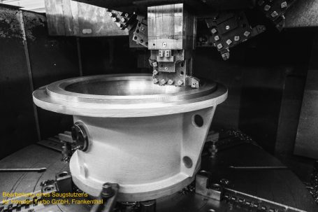 Maschinenbauteil in schwarz-weiß, mit präziser Form und mehreren Befestigungslöchern.